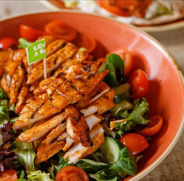 Grilled chicken breast slices over mixed salad greens with cherry tomatoes and cucumber in a ceramic bowl