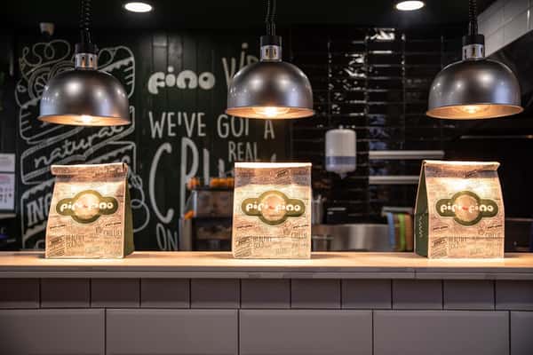 Three branded takeaway bags displayed on a restaurant counter under warm pendant lights inside a modern casual dining space