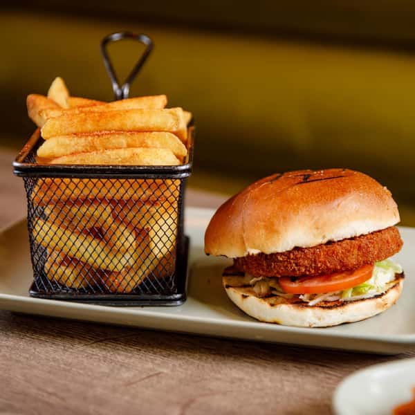 Breaded chicken burger with lettuce and tomato on a toasted bun, served with golden fries in a metal basket on a plate