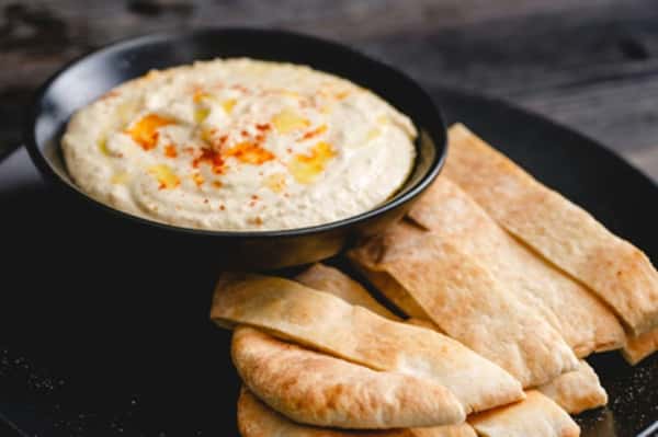 Creamy hummus drizzled with olive oil and paprika served in a black bowl with warm pita bread wedges on a dark plate