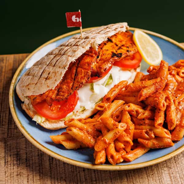 Grilled chicken pita with tomato, lettuce, and creamy sauce served alongside penne pasta in a rich tomato cream sauce