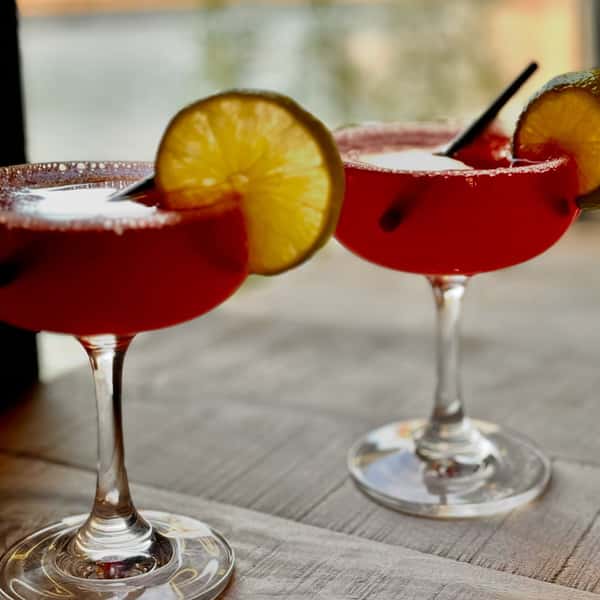 Two red cocktails in coupe glasses garnished with lime slices and sugar rims on a wooden table, softly lit for an elegant presentation