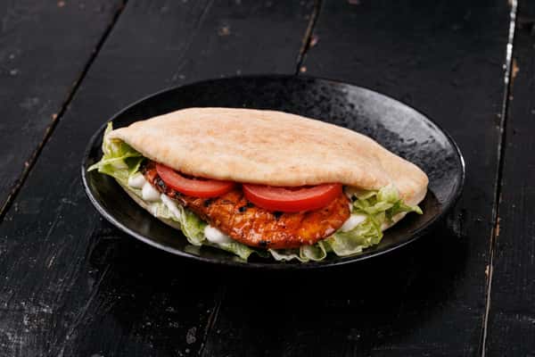 Grilled chicken pita with lettuce, tomato slices, and creamy sauce served on a black plate over a dark wooden table