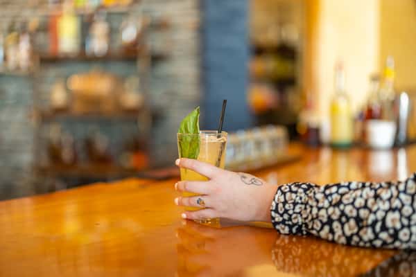Close-up of a guest holding a yellow cocktail garnished with fresh basil and served in a tall glass, resting on a polished wood bar at Sequoia Brewing Company.