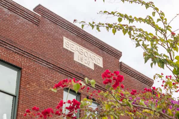 Red brick building with "SEABOARD 1926" engraved on the facade, framed by pink and green flowering branches.