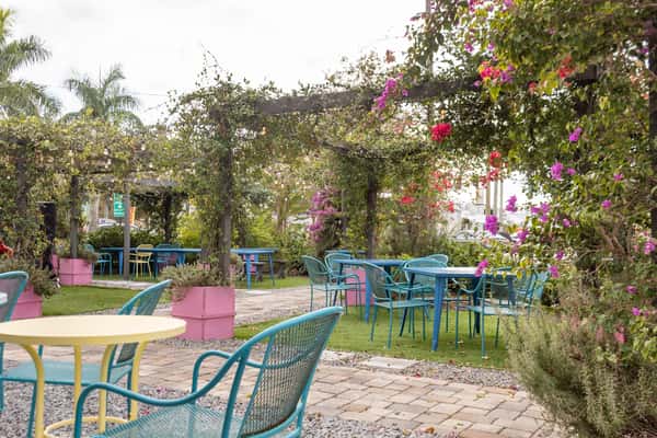 Charming outdoor garden seating area with blue tables, teal chairs, string lights, and blooming pink and purple flowers.