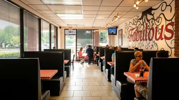 Interior of a casual restaurant with patrons seated in black booths and a large "Fabulous" mural on the wall.