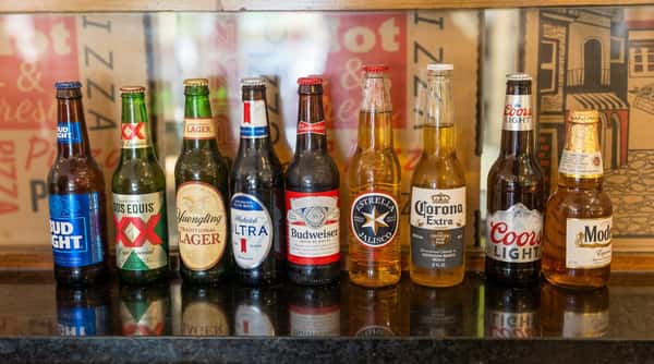 Assorted beer bottles, including Bud Light, Corona, Modelo, and Yuengling, lined up on a black bar top.