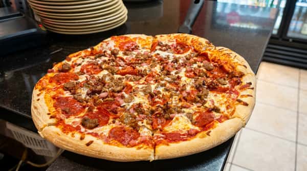 Meat lover's pizza with pepperoni, ham, and sausage, on a dark countertop with a stack of plates.