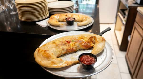 Two crescent-shaped calzones dusted with parmesan, served on metal trays with a side of marinara sauce.
