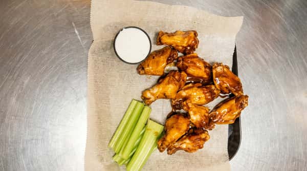 Glazed chicken wings with a side of celery sticks and ranch dressing on wax paper.