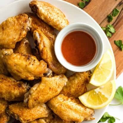 Golden brown plain chicken wings paired with a side of hot sauce and lemon wedges—crispy and juicy appetizer perfect for dipping.