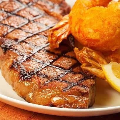 Juicy grilled steak with char marks, served with crispy golden onion rings and a lemon wedge—perfect for classic American steakhouse or surf and turf menus.