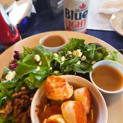 Seared scallops served alongside a fresh spring mix salad with crumbled feta and two sides of dressing—light and protein-rich seafood plate, perfect with a cold beer.