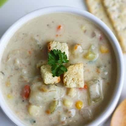 Thick and creamy vegetable chowder with visible chunks of corn, potatoes, carrots, and topped with crunchy croutons and parsley—comforting homemade soup.