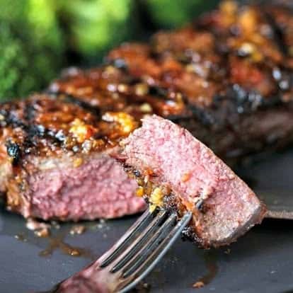 Juicy grilled steak cooked to medium-rare, sliced to reveal a pink center, served with roasted garlic glaze and steamed broccoli—hearty steakhouse meal.