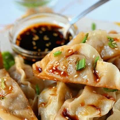 Close-up of pan-fried Asian dumplings garnished with sesame seeds and scallions, served with a side of soy dipping sauce, showcasing authentic Asian appetizer presentation.