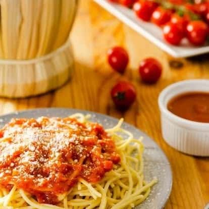 Classic spaghetti topped with savory marinara sauce and grated parmesan cheese, set on a rustic wooden table with fresh cherry tomatoes in the background—traditional Italian pasta dish.