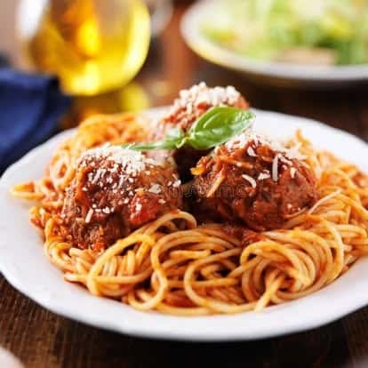 Classic Italian spaghetti with meatballs topped with marinara sauce, grated Parmesan, and fresh basil, served on a white plate in a cozy restaurant setting.