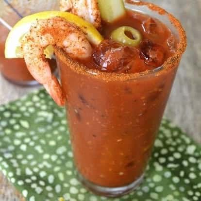 Spicy Bloody Mary cocktail garnished with lemon, olives, and shrimp, served in a salt-rimmed glass—bold brunch drink with savory toppings.