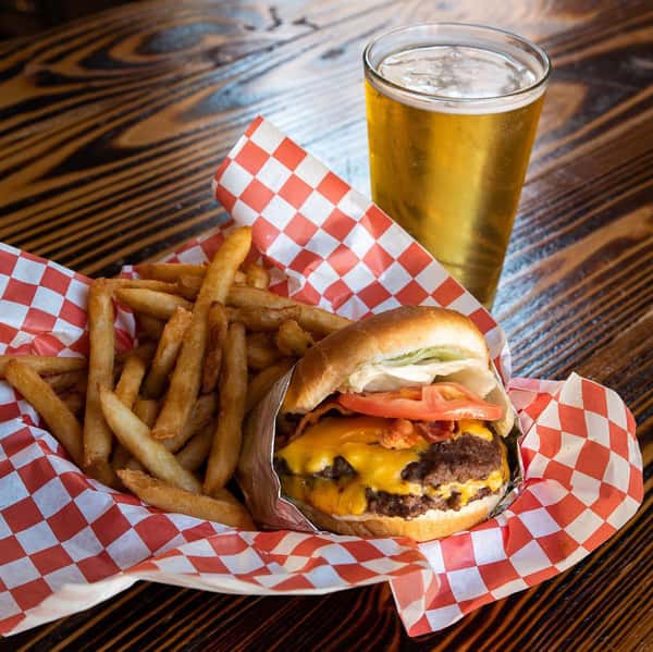Cheeseburger with lettuce and tomato served with fries in a red checkered basket, paired with a pint of cold beer.
