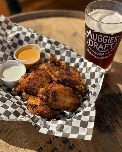 Basket of crispy chicken wings with ranch and buffalo sauces, served with a dark beer on a wooden barrel table.
