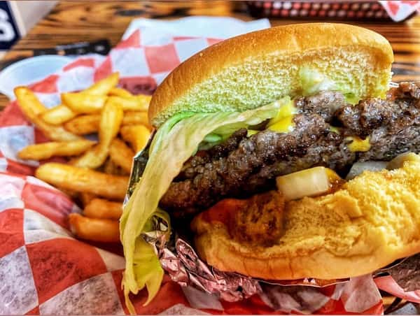 Half-eaten cheeseburger with lettuce, onions, and mustard, served with golden fries in a red checkered basket.