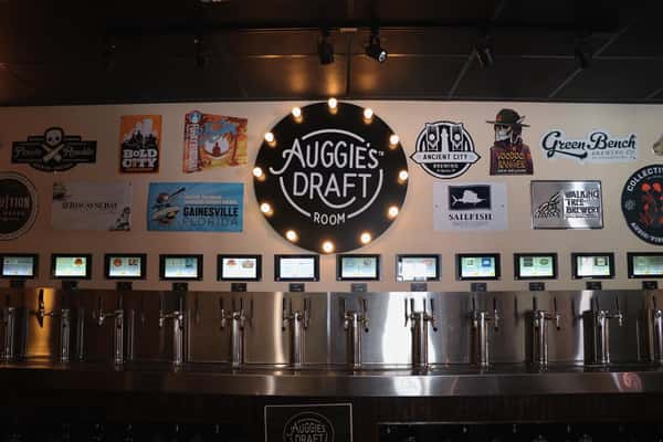 Wall of self-serve beer taps beneath digital menus and brewery signs at Auggie's Draft Room.