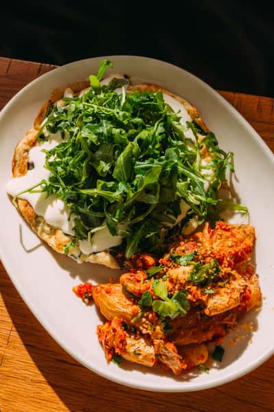 Plated brunch entrée with a fluffy egg white omelette topped with arugula and creamy cheese, served alongside roasted fingerling potatoes in tomato herb sauce.