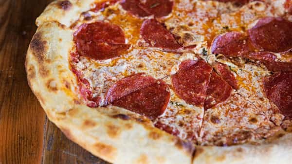 Close-up of a freshly baked pepperoni pizza with a golden, blistered crust and melted cheese, resting on a wooden surface.