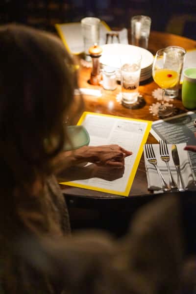 Customer browsing a dinner menu at a cozy restaurant table set with drinks, silverware, and ambient lighting for an intimate dining experience.