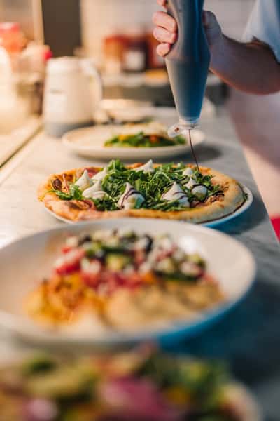 Freshly baked arugula and burrata pizza drizzled with balsamic glaze on a marble counter in a modern Italian restaurant kitchen.