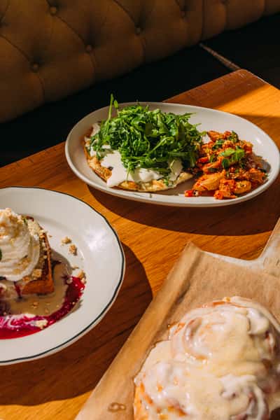 Flatbread pizza topped with creamy cheese and arugula served with spicy roasted potatoes, alongside a cinnamon roll and plated French toast.