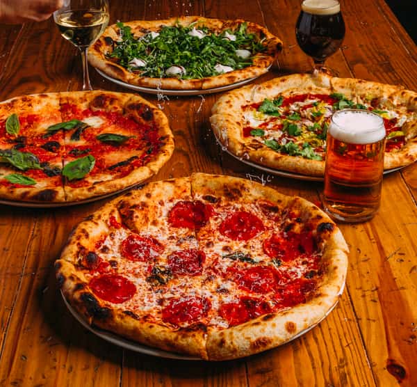 Variety of artisan pizzas including pepperoni, margherita, burrata arugula, and spicy cilantro-topped pie, served with craft beer and white wine on a rustic wooden table at a trendy pizzeria