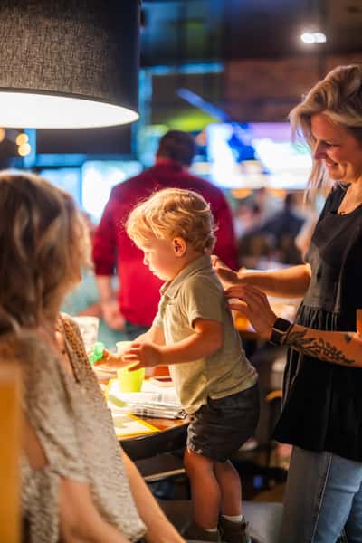 Family-friendly dining scene with a young child standing on a chair, smiling and interacting with family members in a lively restaurant setting.