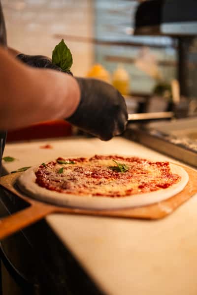 A chef is preparing pizza dough with sauce, cheese, and fresh basil.