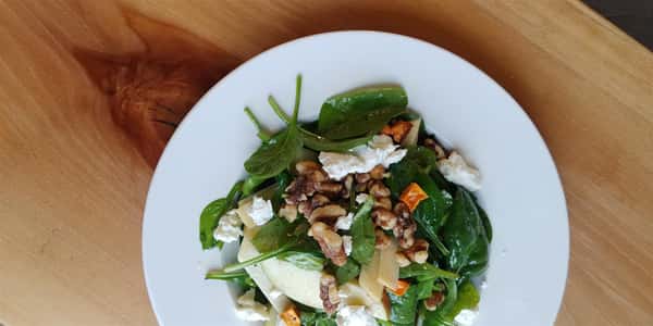 a salad with spinach, sliced apples, rutabaga, walnuts, sweet potatoes, and goat cheese tossed in a honey vinaigrette