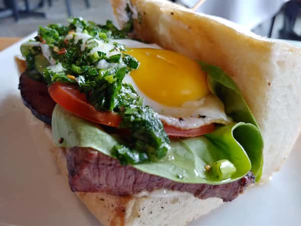 Steak sandwich topped wit lettuce, tomato, and a sunny side up egg