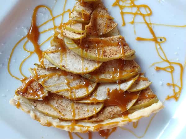 A slice of apple pie topped with cooked apples and a caramel drizzle