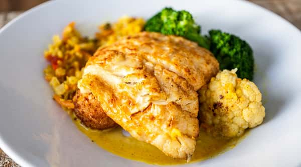 Pan-seared fish fillet with turmeric-spiced rice, broccoli, and yellow cauliflower on a white plate