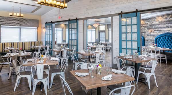 Restaurant interior with distressed white metal chairs, wooden tables, and blue barn doors separating sections
