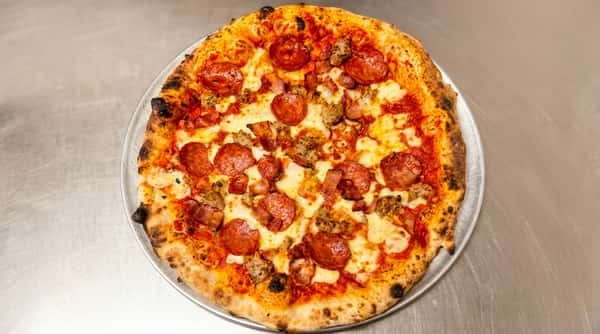 Meat lover's pizza with pepperoni, sausage, bacon, and melted mozzarella on a metal tray.
