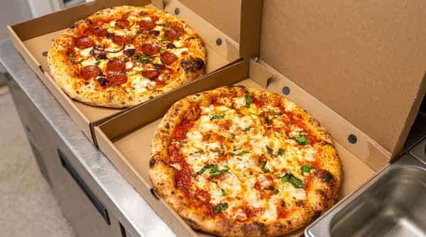 Two pizzas in cardboard boxes: a pepperoni and onion pizza, and a Margherita pizza with basil.