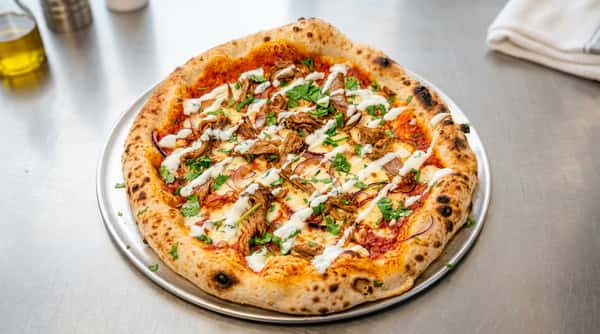 Pizza with shredded meat, red onion, melted cheese, green herbs, and white sauce drizzle.