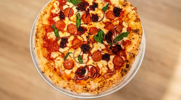Pepperoni pizza with red onion, basil, mozzarella, and chili crisp on a metal pan.
