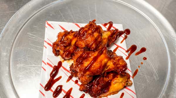 BBQ chicken wings drizzled with sauce on striped paper, on a metal surface.