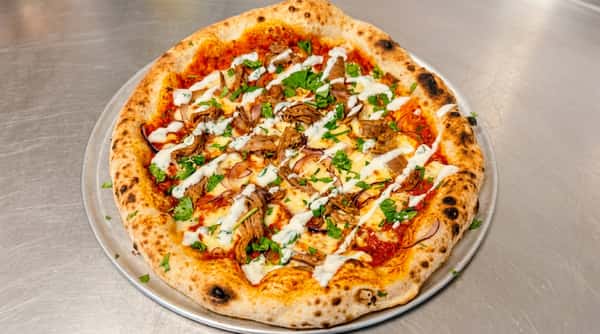 Pizza with shredded meat, red onion, melted cheese, green herbs, and white sauce drizzle.
