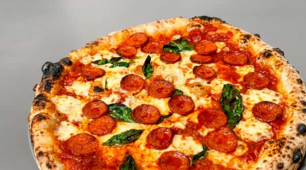 Pepperoni pizza with melted mozzarella, red sauce, green basil, and a charred crust.