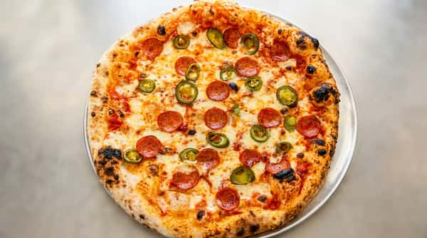 Pepperoni and jalapeño pizza with melted mozzarella cheese and a charred crust on a metal pan.