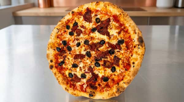 Pizza with melted cheese, tomato sauce, black olives, and sun-dried tomatoes on a stainless steel counter.